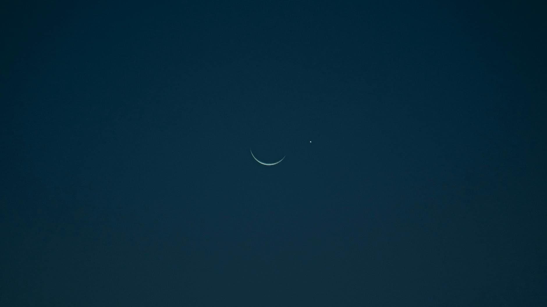 A serene crescent moon and bright planet set against a dark night sky.