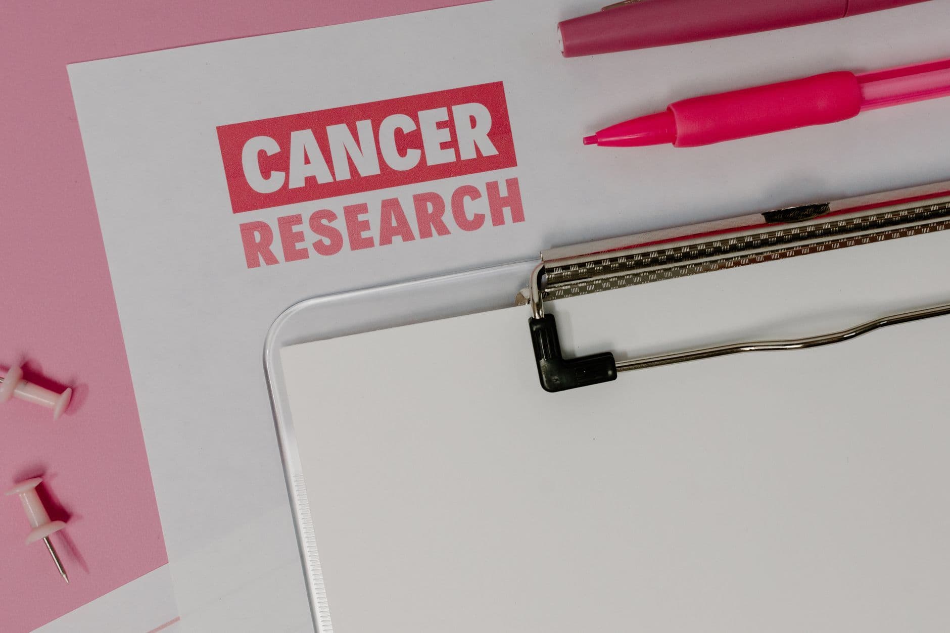 Flat lay of a cancer research paper on a clipboard with pink stationery items.