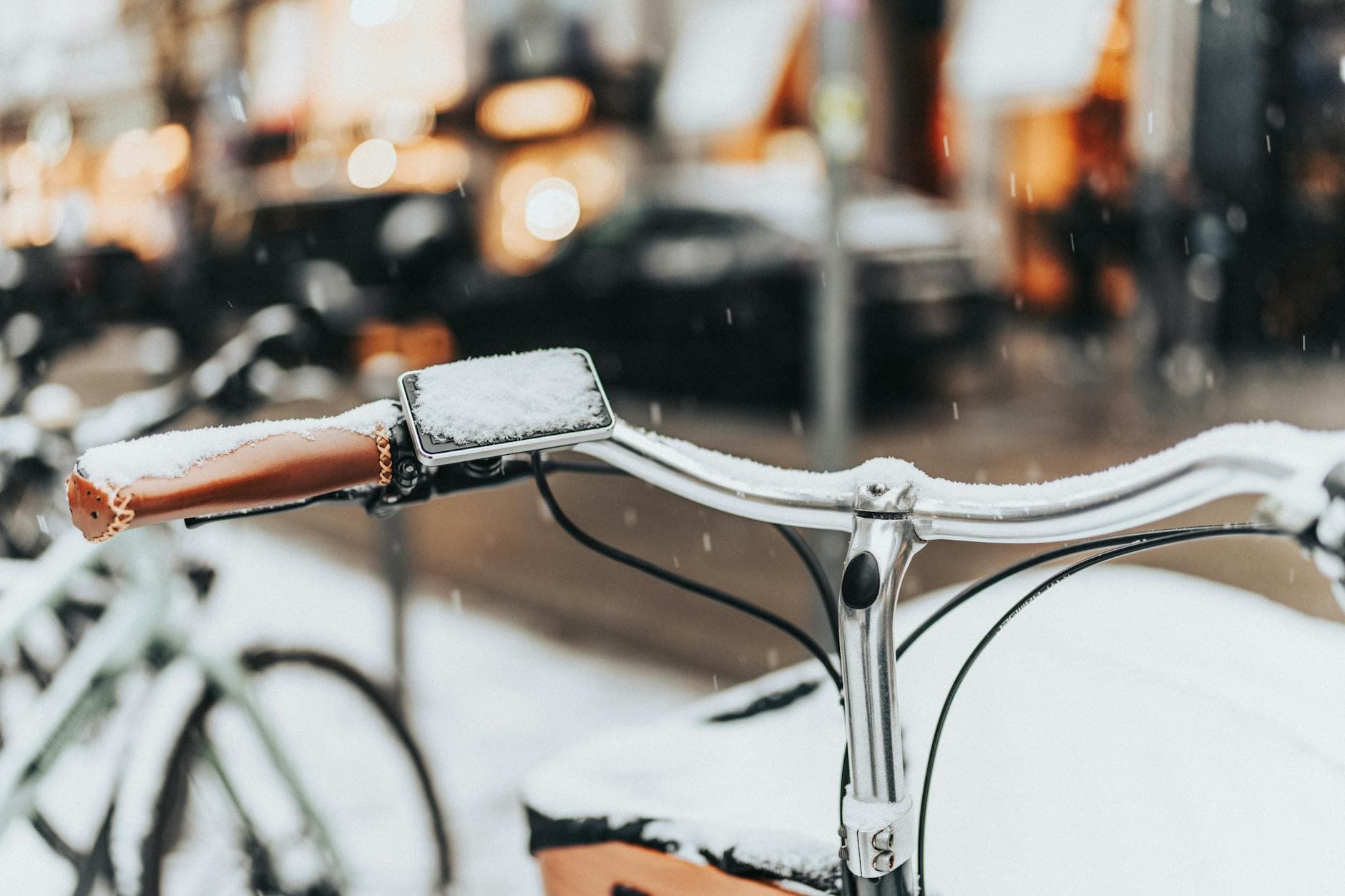 Close-up of a bicycle handlebar dusted with snow on a city street. Urban winter atmosphere.