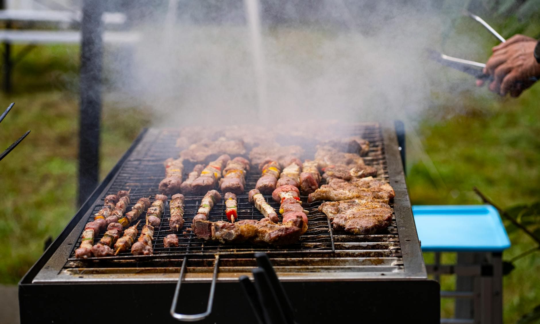 A smoky outdoor barbecue in Switzerland featuring skewered meats cooking on a grill.