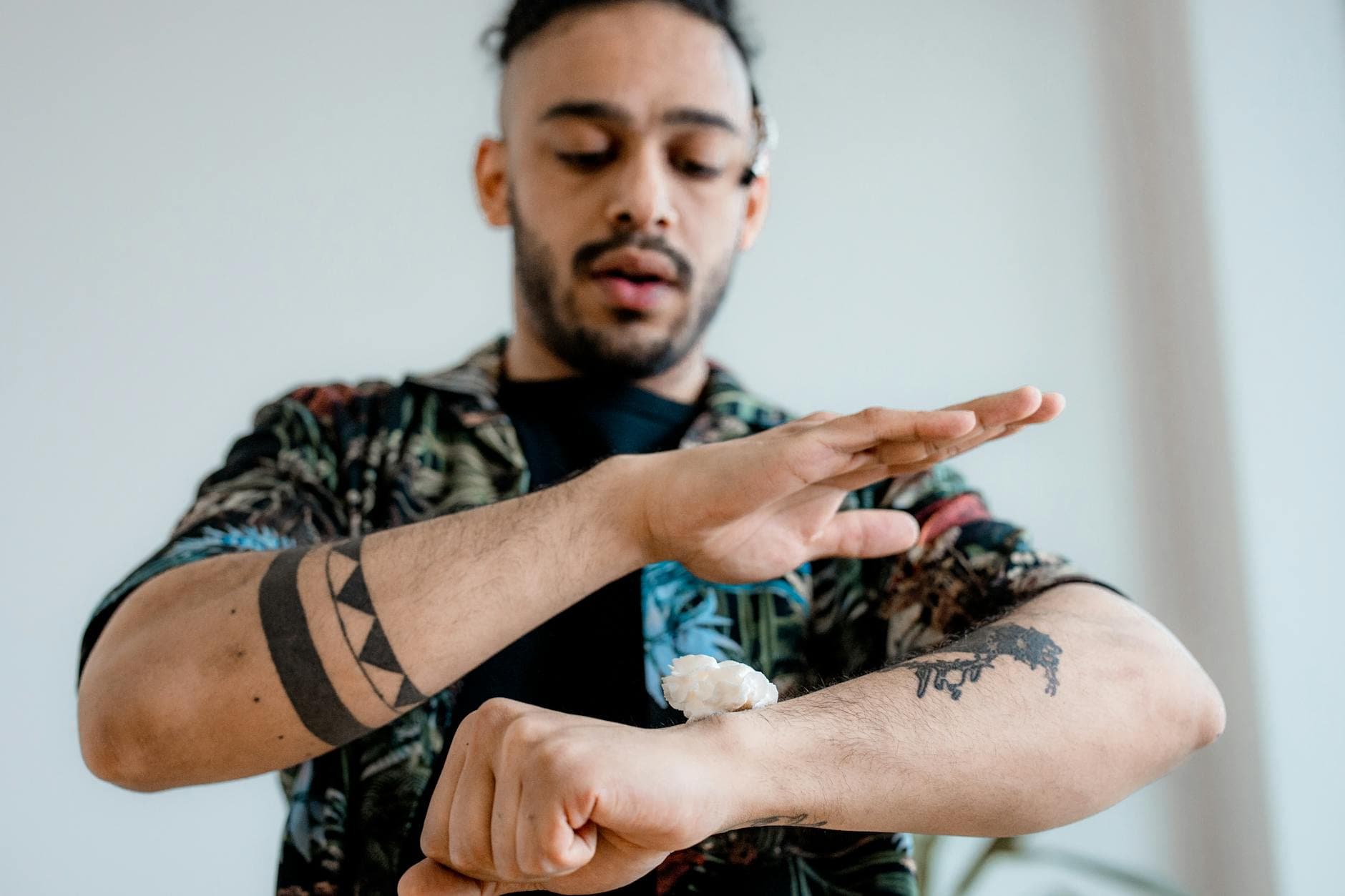 A man with tattoos applies cream to his forearm, highlighting tattoo care and skincare routines.