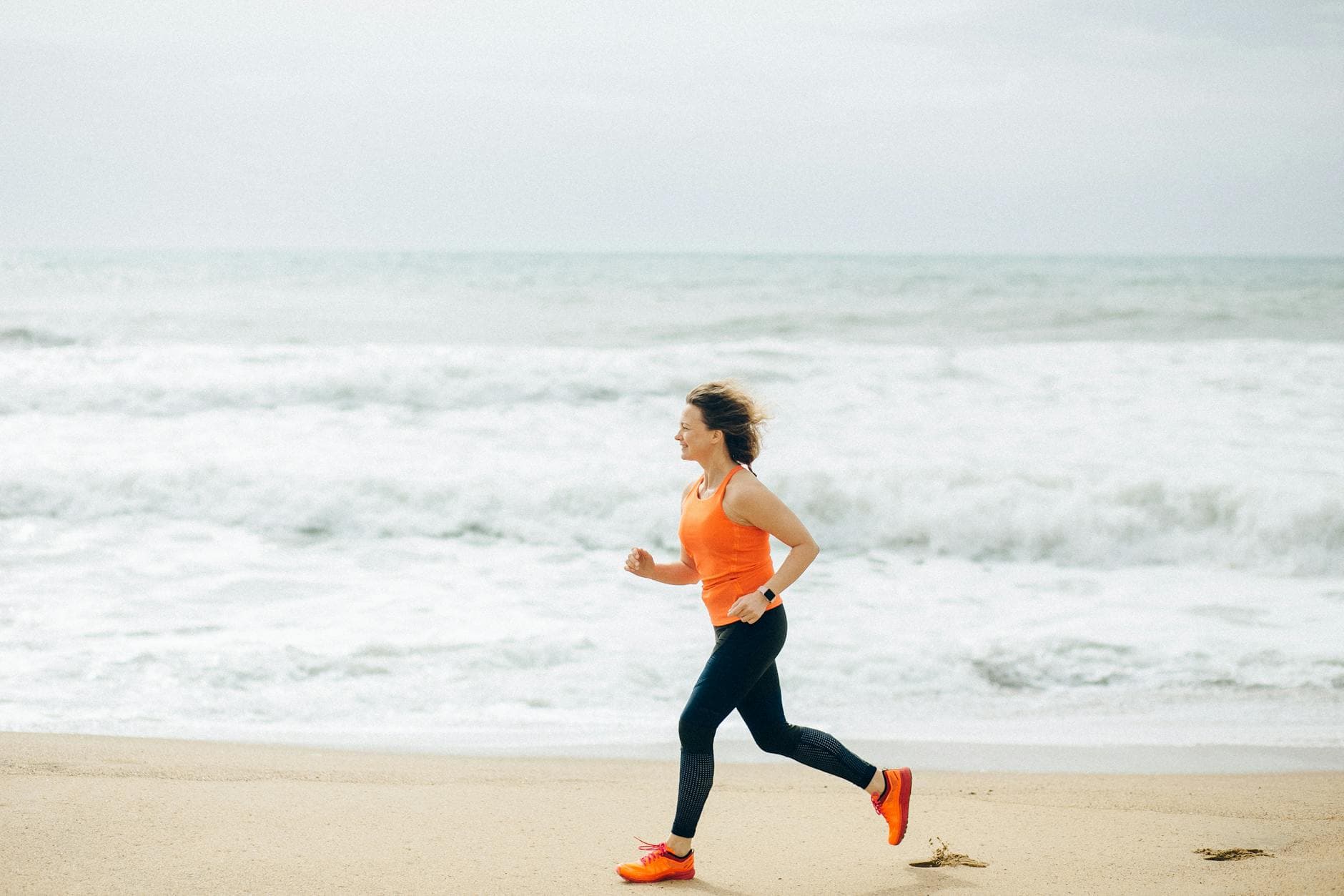 Fit woman running on the sandy beach by the ocean, embracing an active lifestyle.