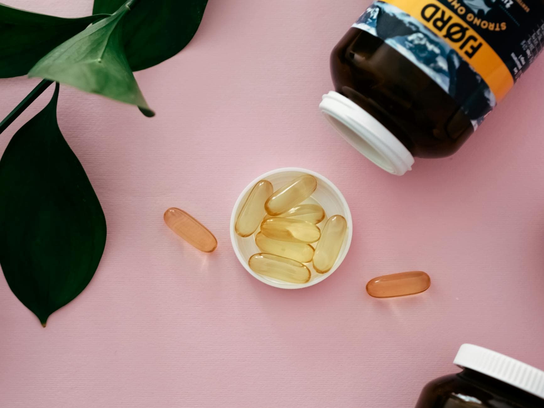 Top view of cod liver oil capsules in a bottle cap on a pink background.